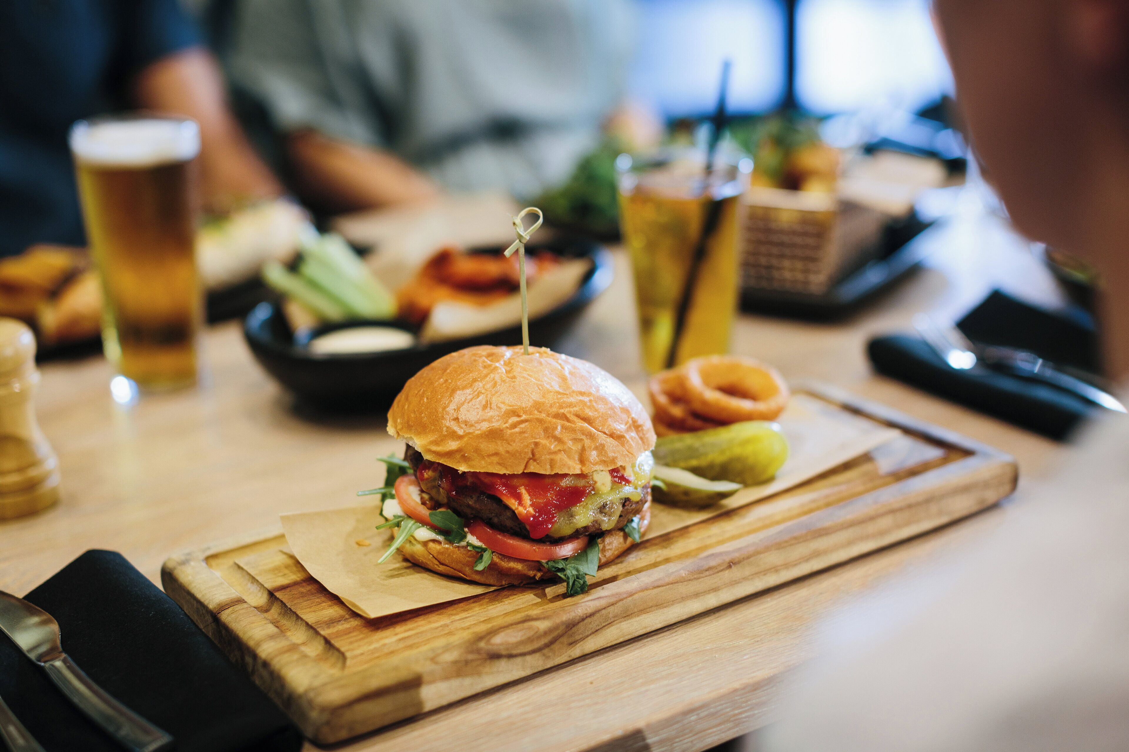 A burger on a wooden board with a knife and fork beside it.