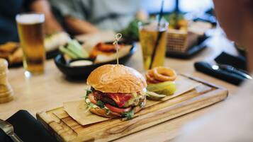 A burger on a wooden board with a knife and fork beside it.