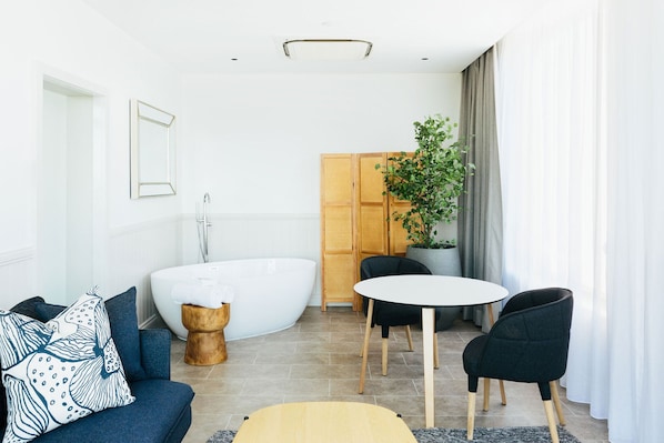 A modern bathroom with a freestanding bathtub, a wooden stool, and a potted plant.