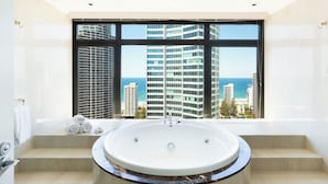 A modern bathroom with a large bathtub, a view of tall buildings, and a clear sky. - Voco Gold Coast (Surfers Paradise)