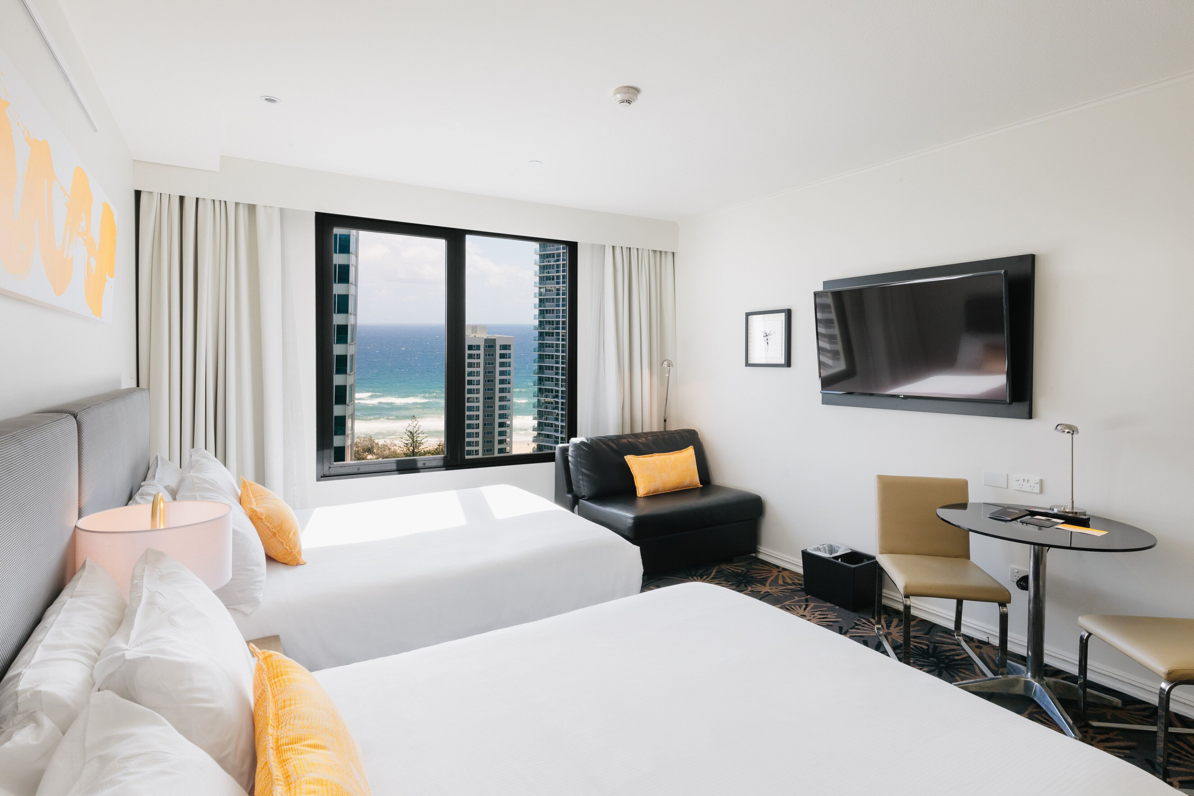 A hotel room with a bed, a chair, a desk, a TV, and a view of the ocean.