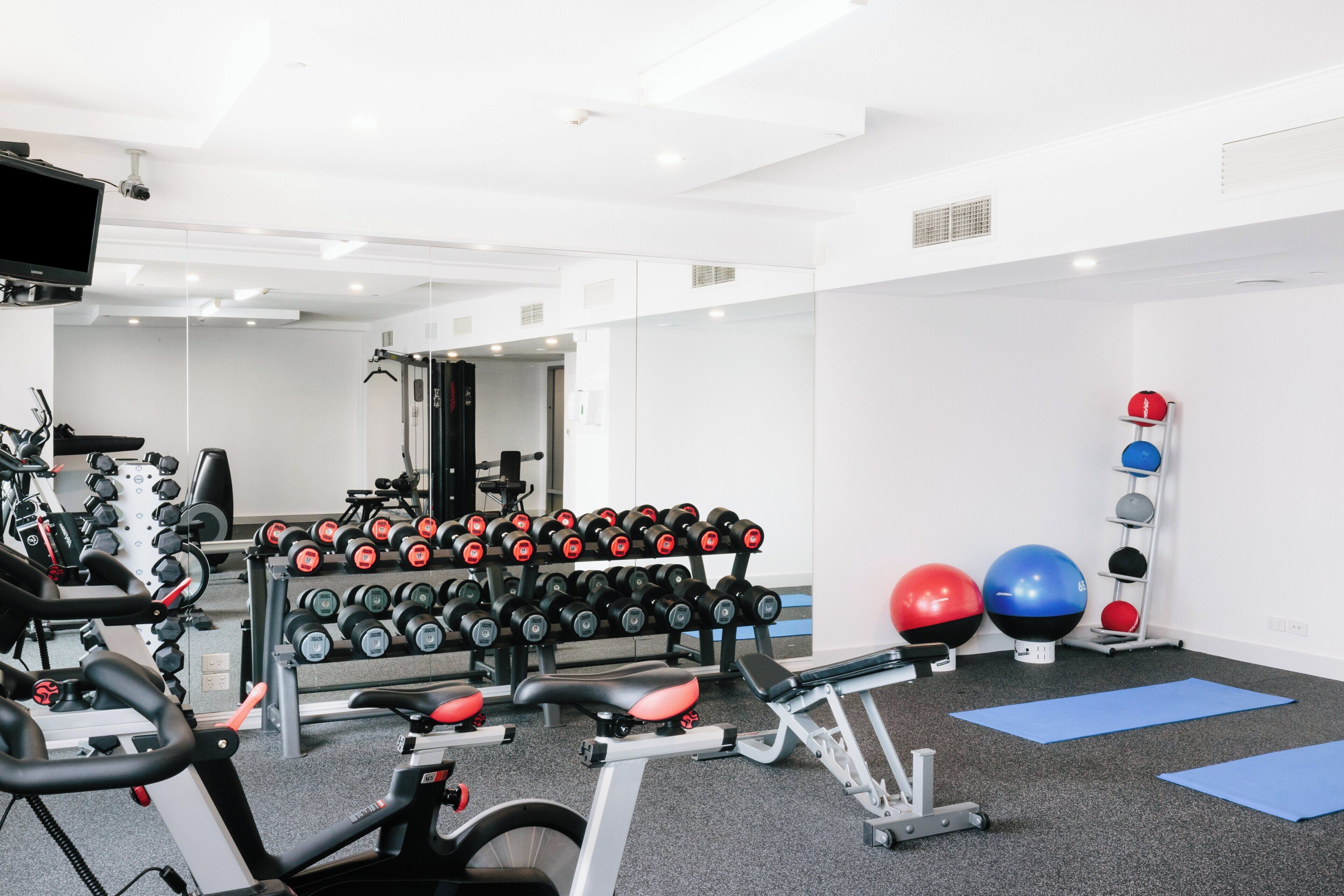Une salle de sport équipée de matériel d’exercice, notamment des haltères, un tapis de course et des ballons d’exercice.
