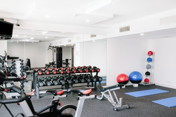 Une salle de sport équipée de matériel d’exercice, notamment des haltères, un tapis de course et des ballons d’exercice.