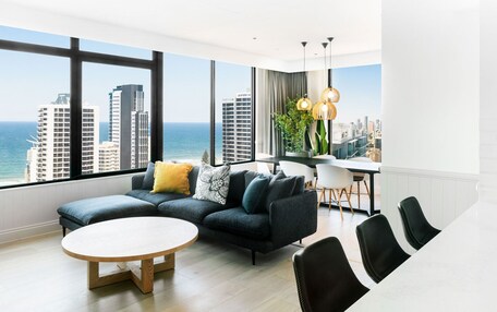 A modern living room with a large window, a sectional sofa, a round coffee table, and a dining area with chairs and a table.