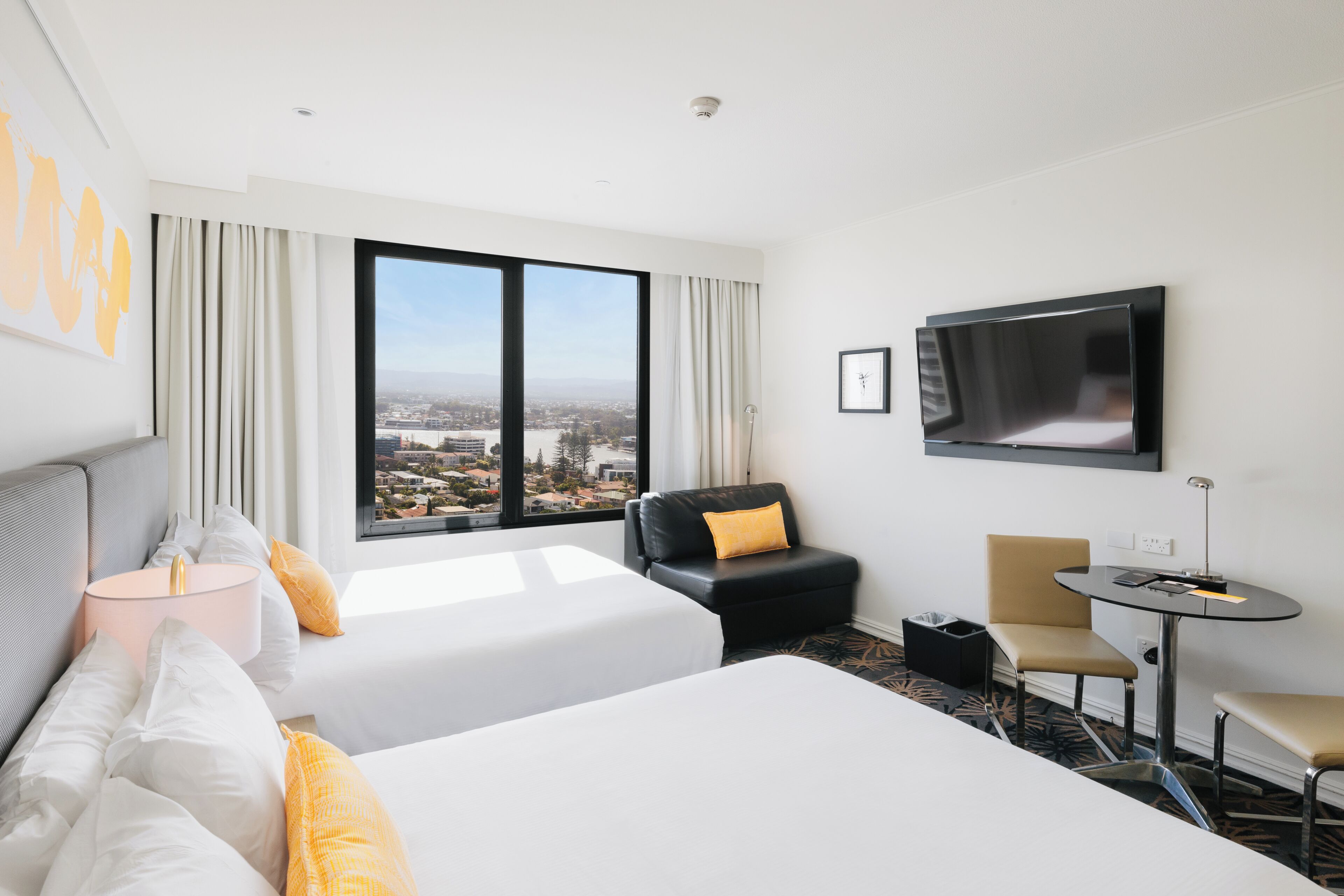 A hotel room with two beds, a TV, a desk, and a view of the city.