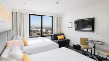 A hotel room with two beds, a TV, a desk, and a view of the city.