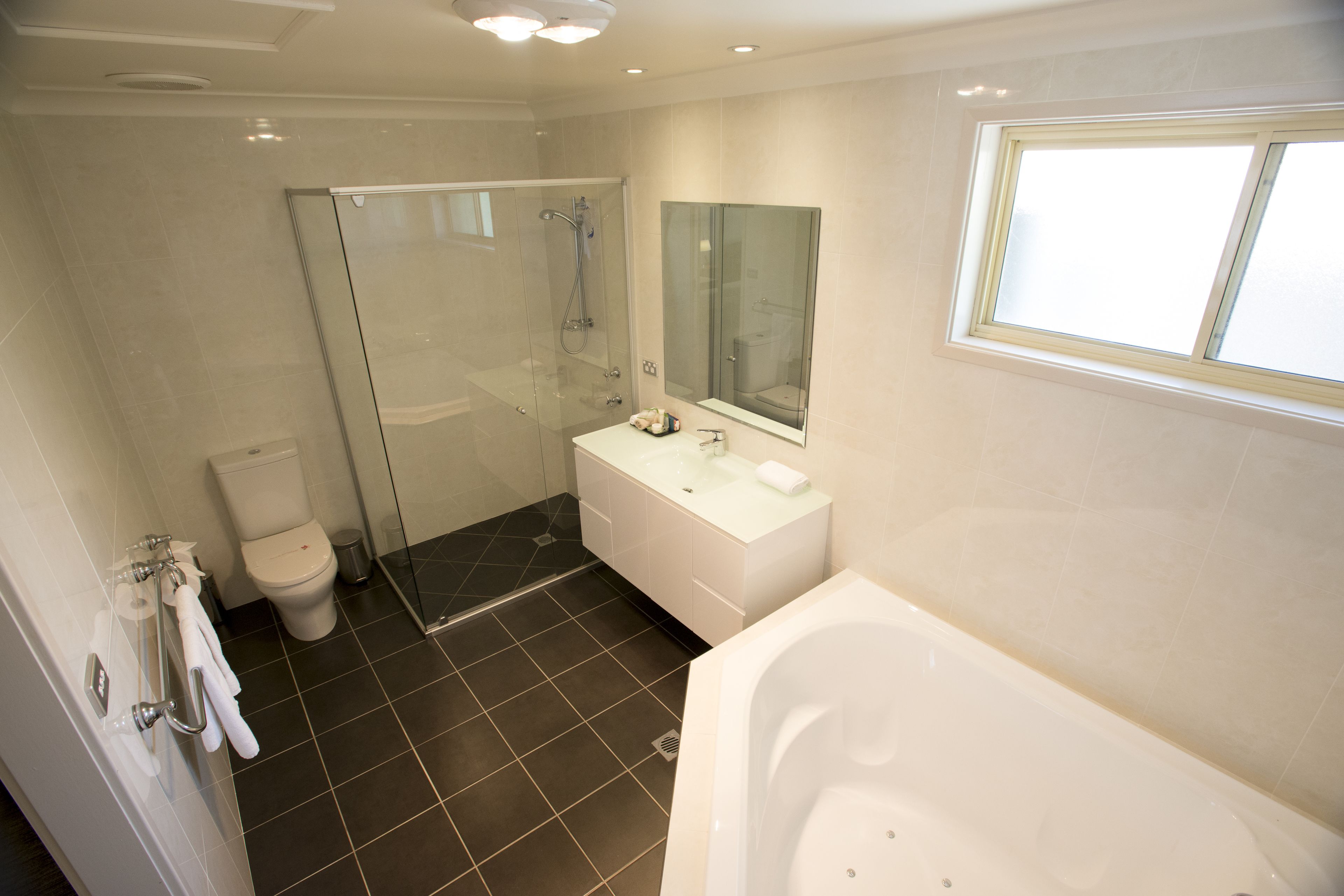 Een moderne badkamer met een glazen douchecabine, een wit toilet, een witte wastafel met een spiegel erboven en een ruime badkuip.