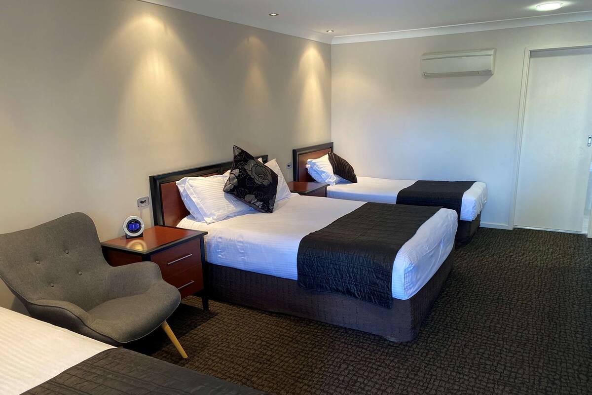 A hotel room with two beds, a desk, a chair, and a clock.