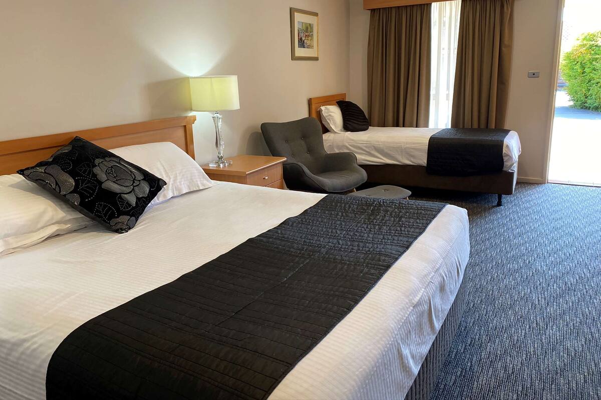 A hotel room with two beds, a chair, a nightstand, a lamp, and a window with curtains.