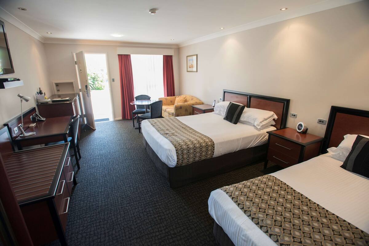 A hotel room with two beds, a desk, a chair, a small table, and a window with curtains.