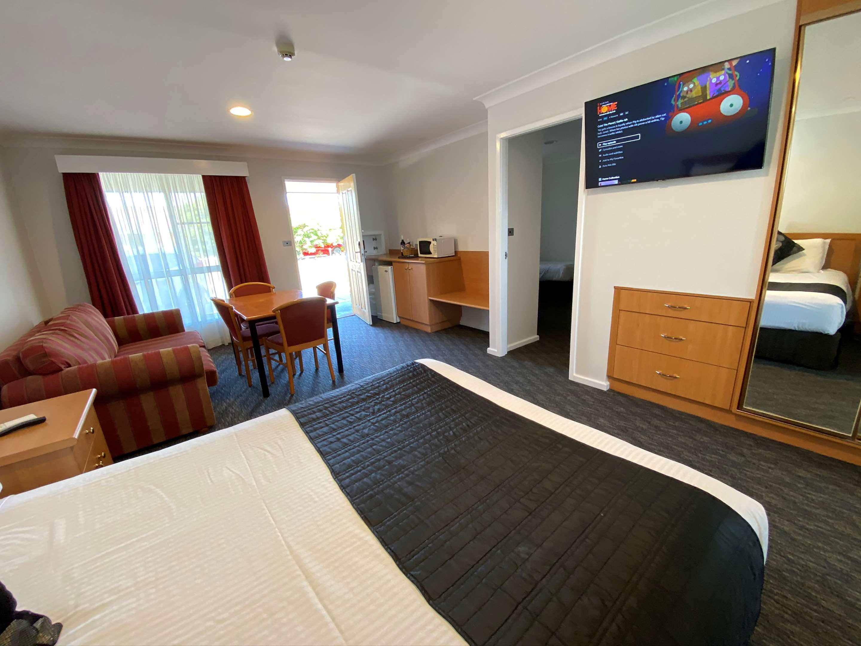 Habitación de hotel con cama, escritorio, silla, televisor, armario y una pequeña kitchenette.