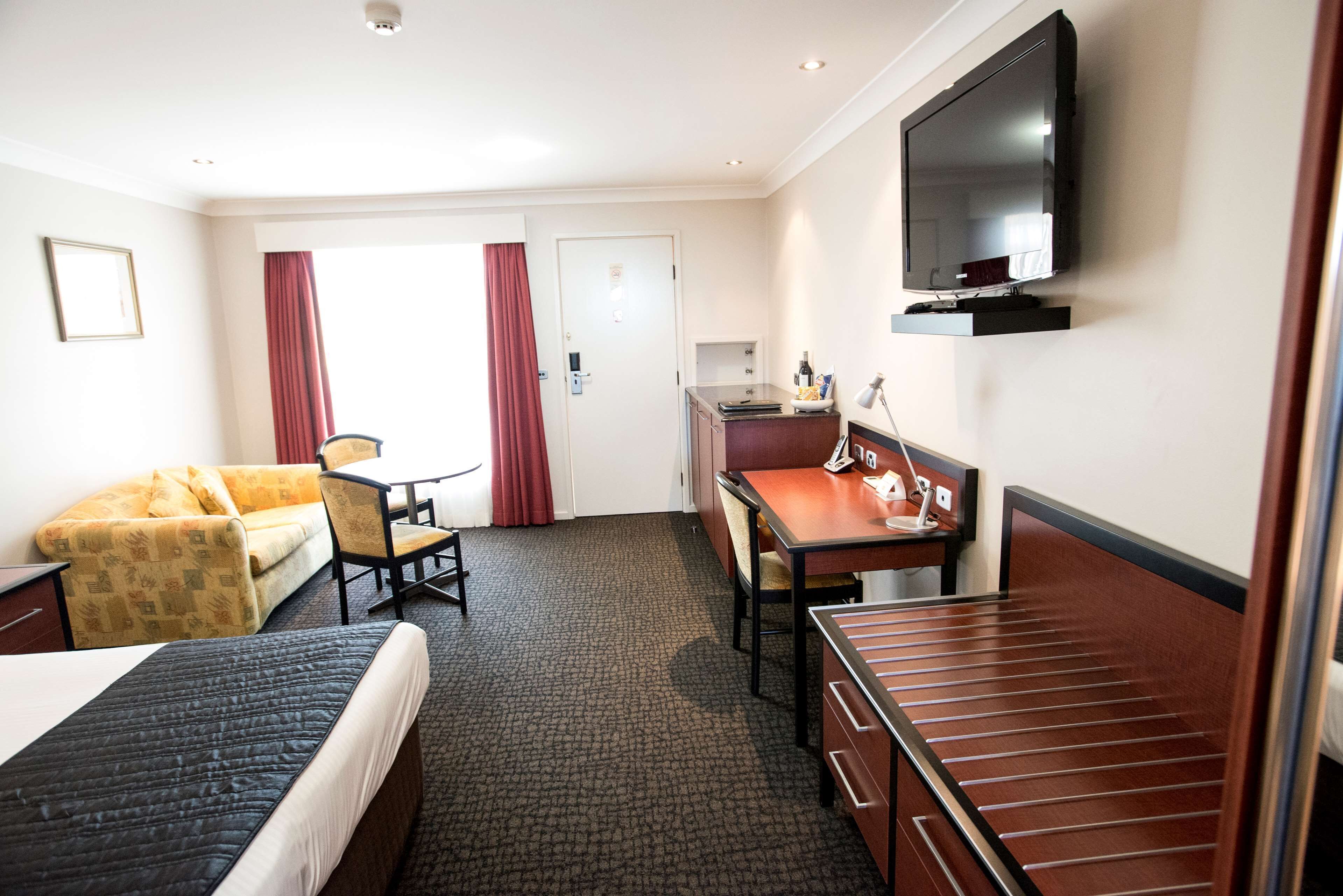 Une chambre d’hôtel comprenant un lit, un canapé, un bureau avec une chaise, une télévision et une fenêtre avec des rideaux.