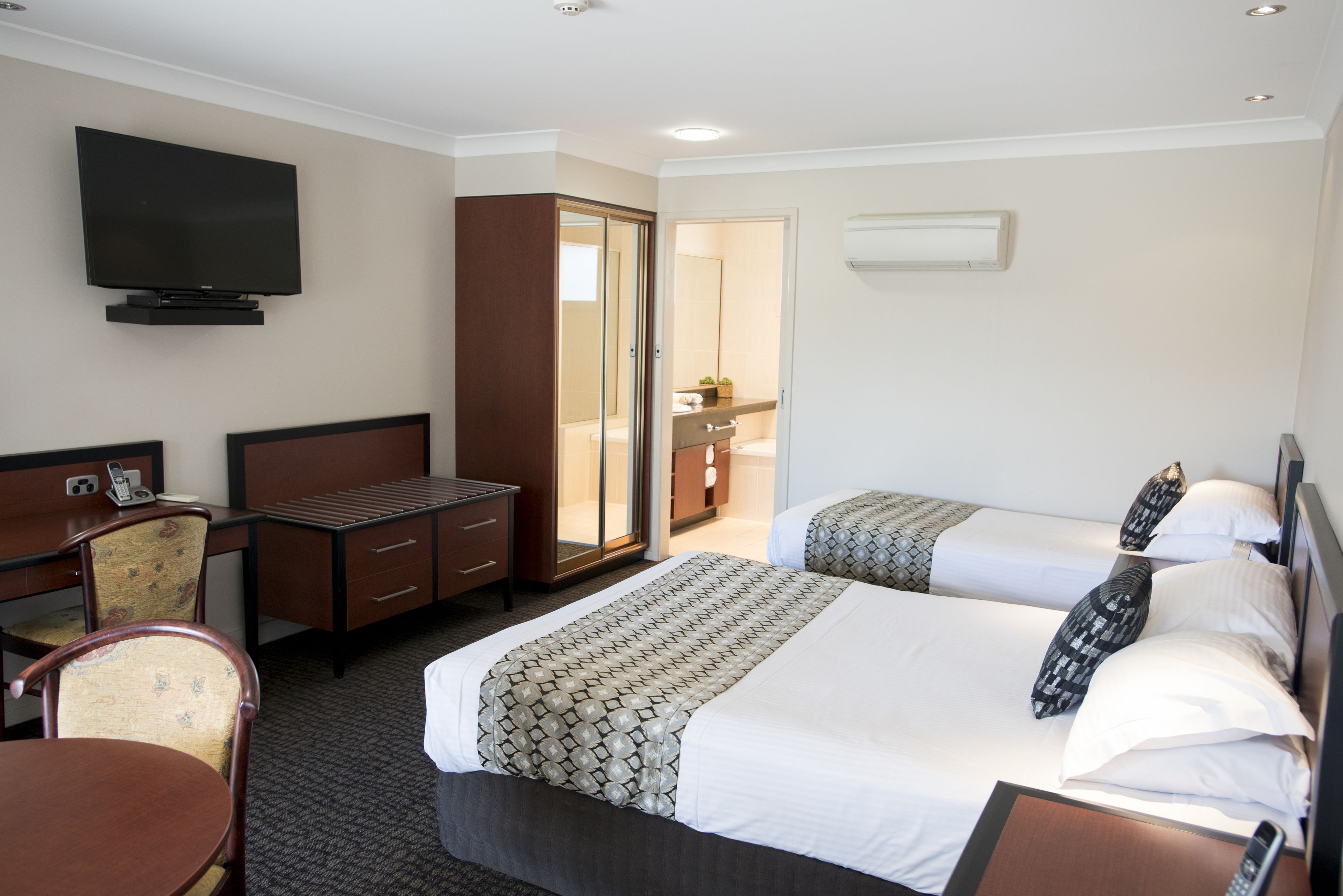 A hotel room with a bed, a desk, a chair, a television, and a bathroom visible through an open door.