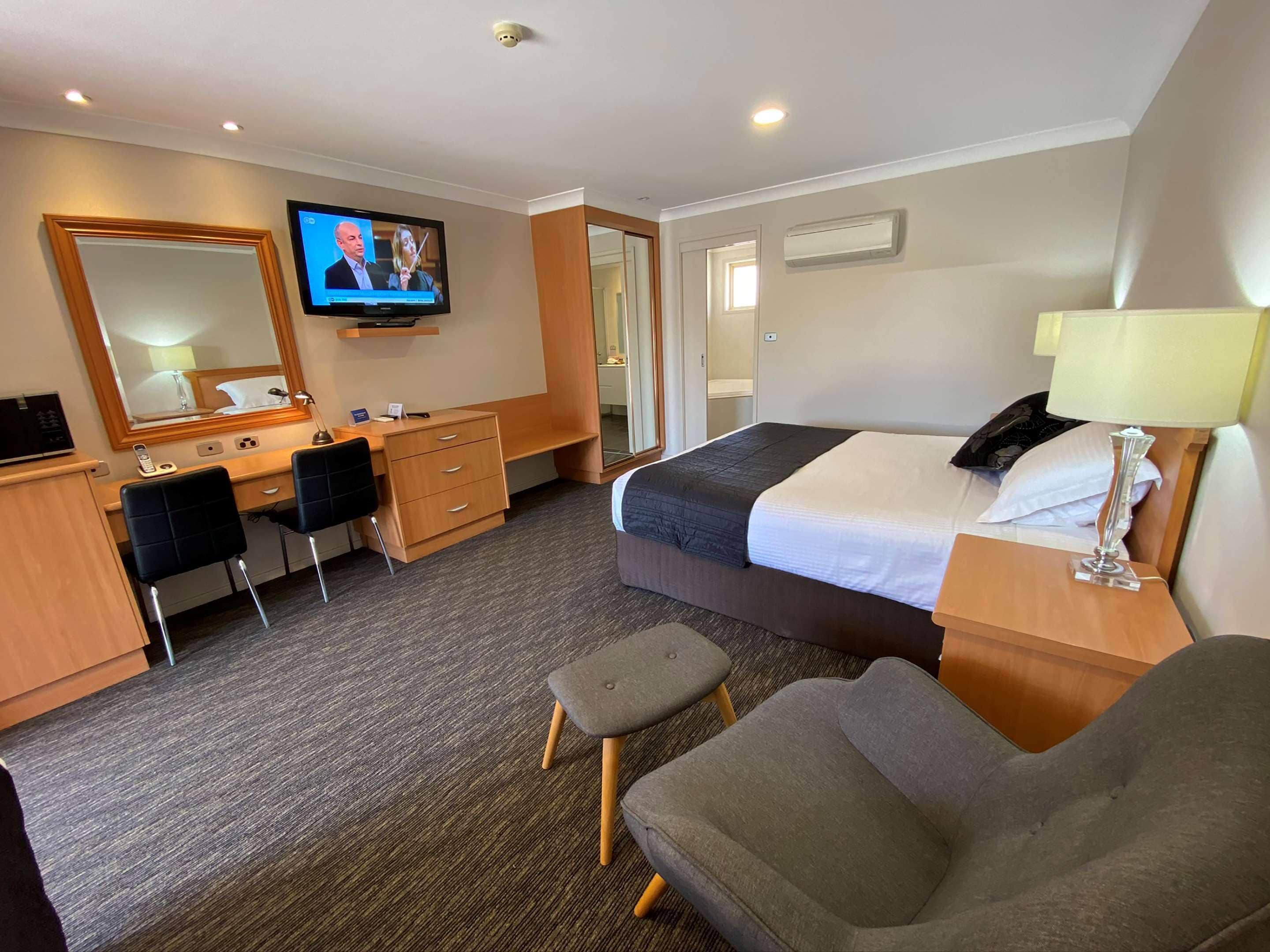 A hotel room with a bed, a desk, a chair, a television, and a mirror.