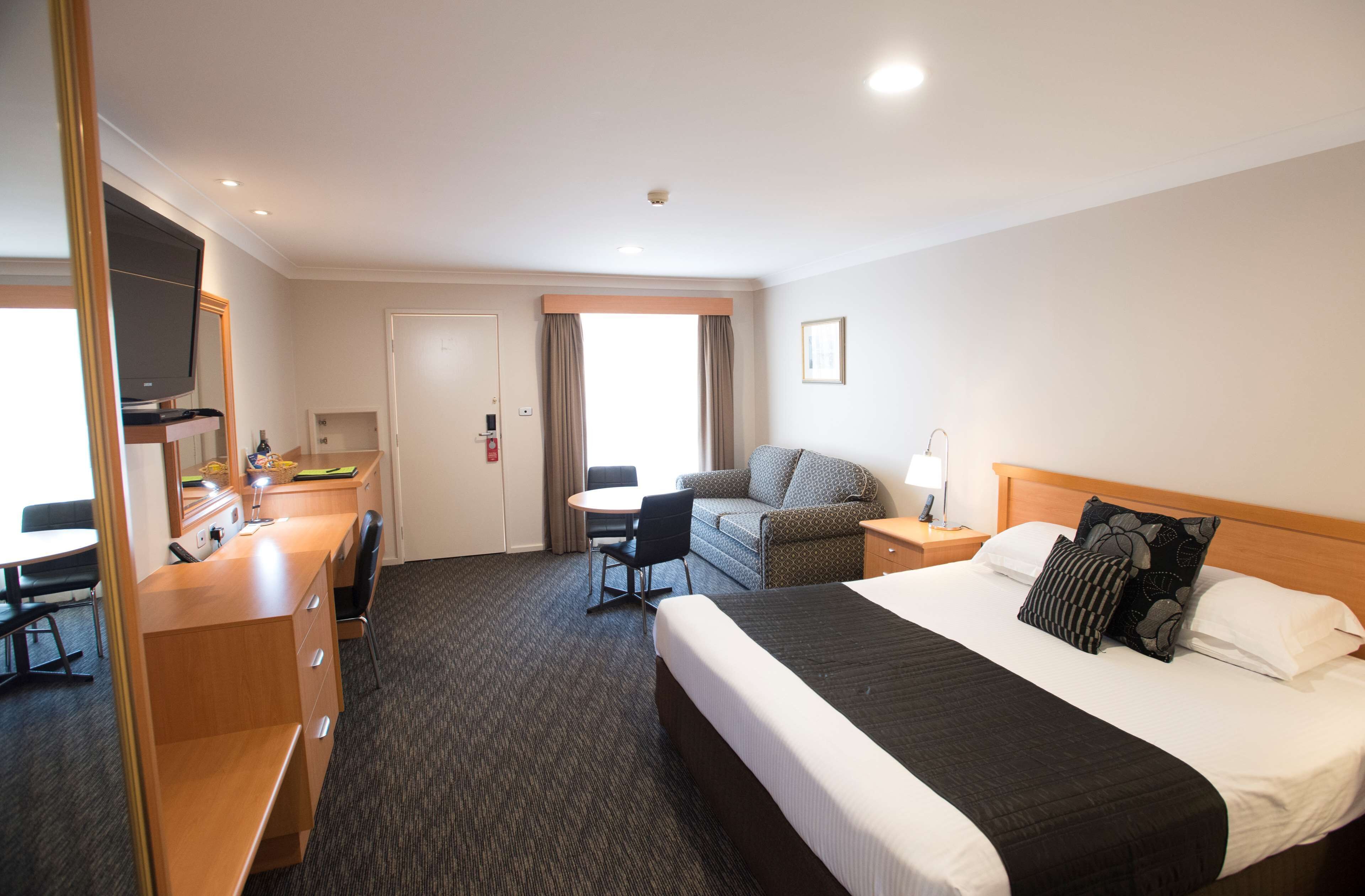 A hotel room with a bed, a desk with a chair, a television, and a window with curtains.