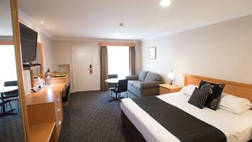 A hotel room with a bed, a desk with a chair, a television, and a window with curtains.