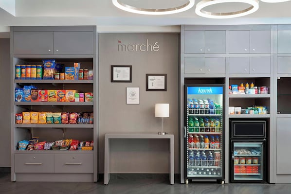 A kitchenette area with shelves stocked with snacks, a refrigerator, and a small table with a lamp.