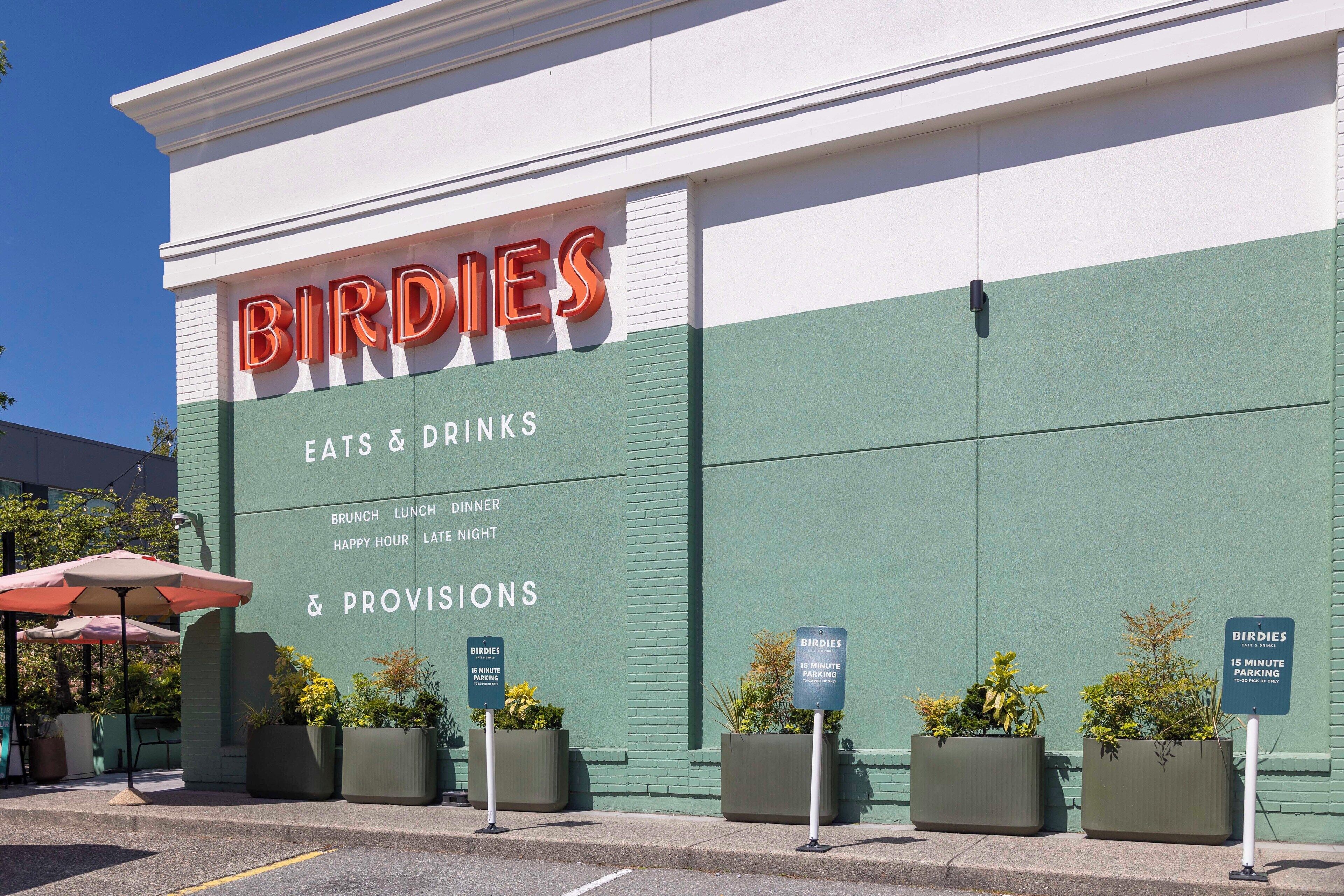 A building with a sign reading "Birdies" and a list of services including eats, drinks, and provisions. There are parking signs indicating 15-minute parking.
