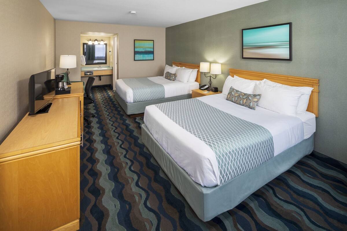 A hotel room with two beds, a desk, a TV, and a bathroom mirror.