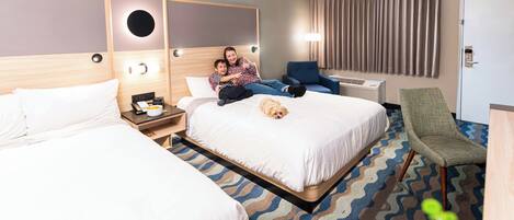 Habitación de hotel con dos camas, un escritorio, una silla y un perro en la cama.