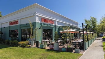 A building with a green and white exterior, the name 'BIRDIES' in red letters, outdoor seating with umbrellas, and potted plants.