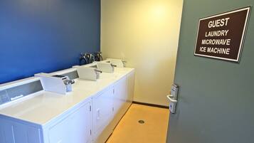 Baño de huéspedes con pared azul, lavamanos blanco y señal que indica la disponibilidad de lavandería para huéspedes, microondas y máquina de hielo.
