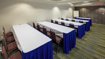 A conference room with multiple tables and chairs, a whiteboard, and a carpeted floor.
