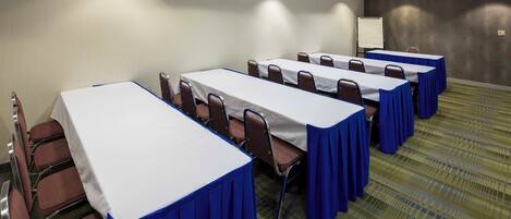 Un salón de conferencias con varias mesas y sillas, una pizarra y piso alfombrado.