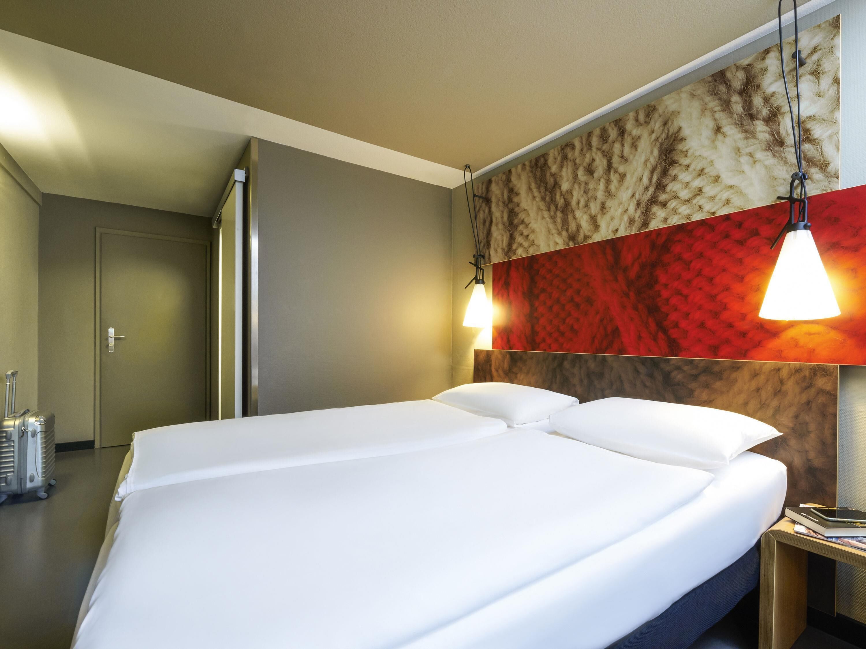 Habitación de hotel con una cama grande, dos lámparas de noche, un cabecero de madera y un calentador de pared.