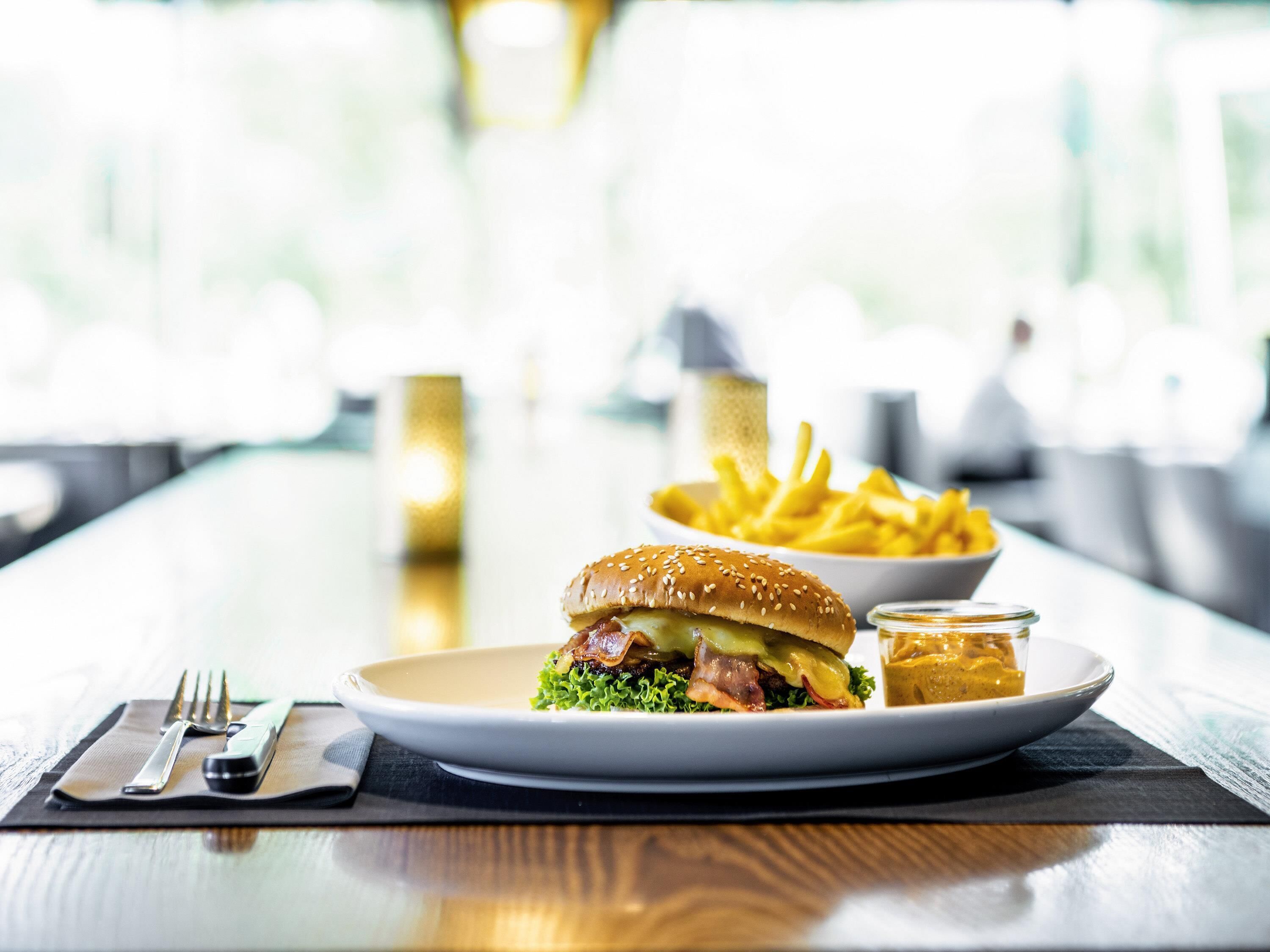 Een maaltijd bestaande uit een hamburger, friet en een klein bakje saus op een tafel.