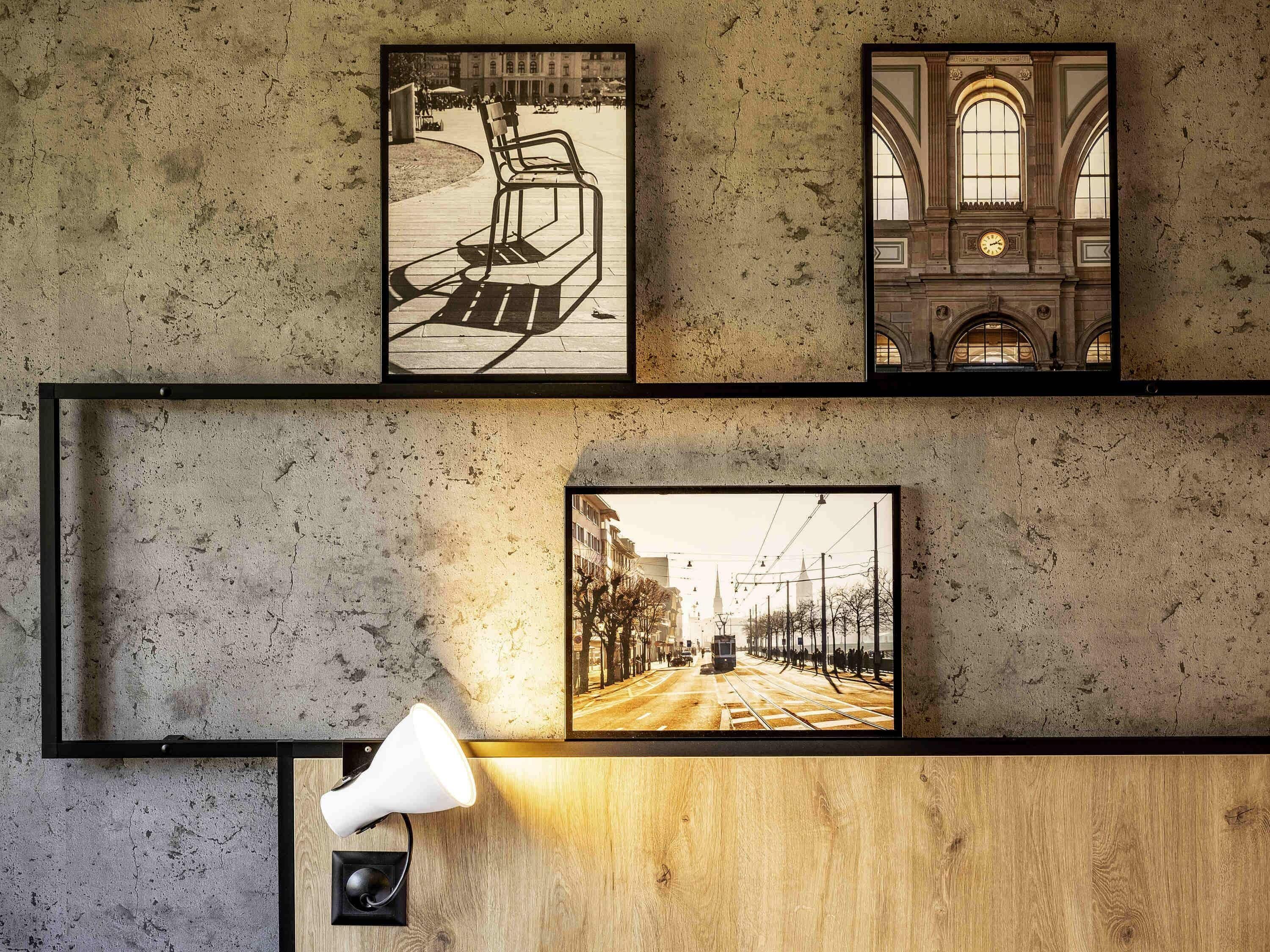 Un mur orné de trois tableaux encadrés : un banc, un bâtiment avec des arcades et une scène de rue.