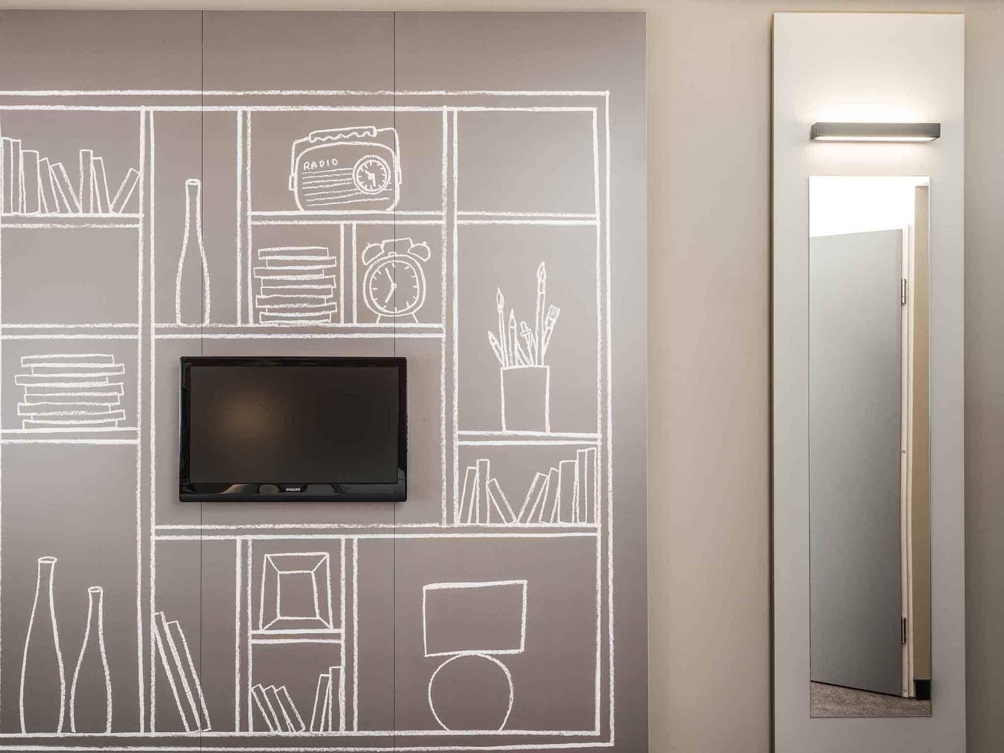 Une chambre moderne avec un téléviseur à écran plat fixé sur un mur recouvert d’un tableau noir, un miroir et une porte.