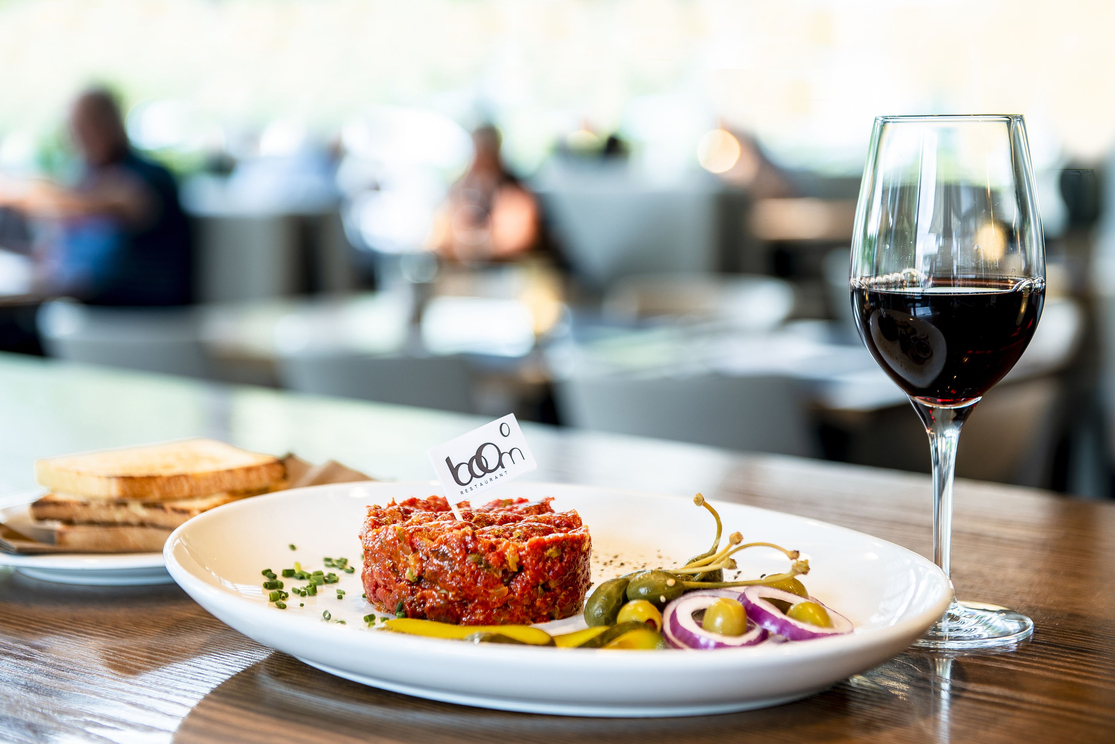 A plate with a meat dish, pickles, and a glass of red wine on a wooden table.