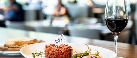 A plate with a meat dish, pickles, and a glass of red wine on a wooden table.