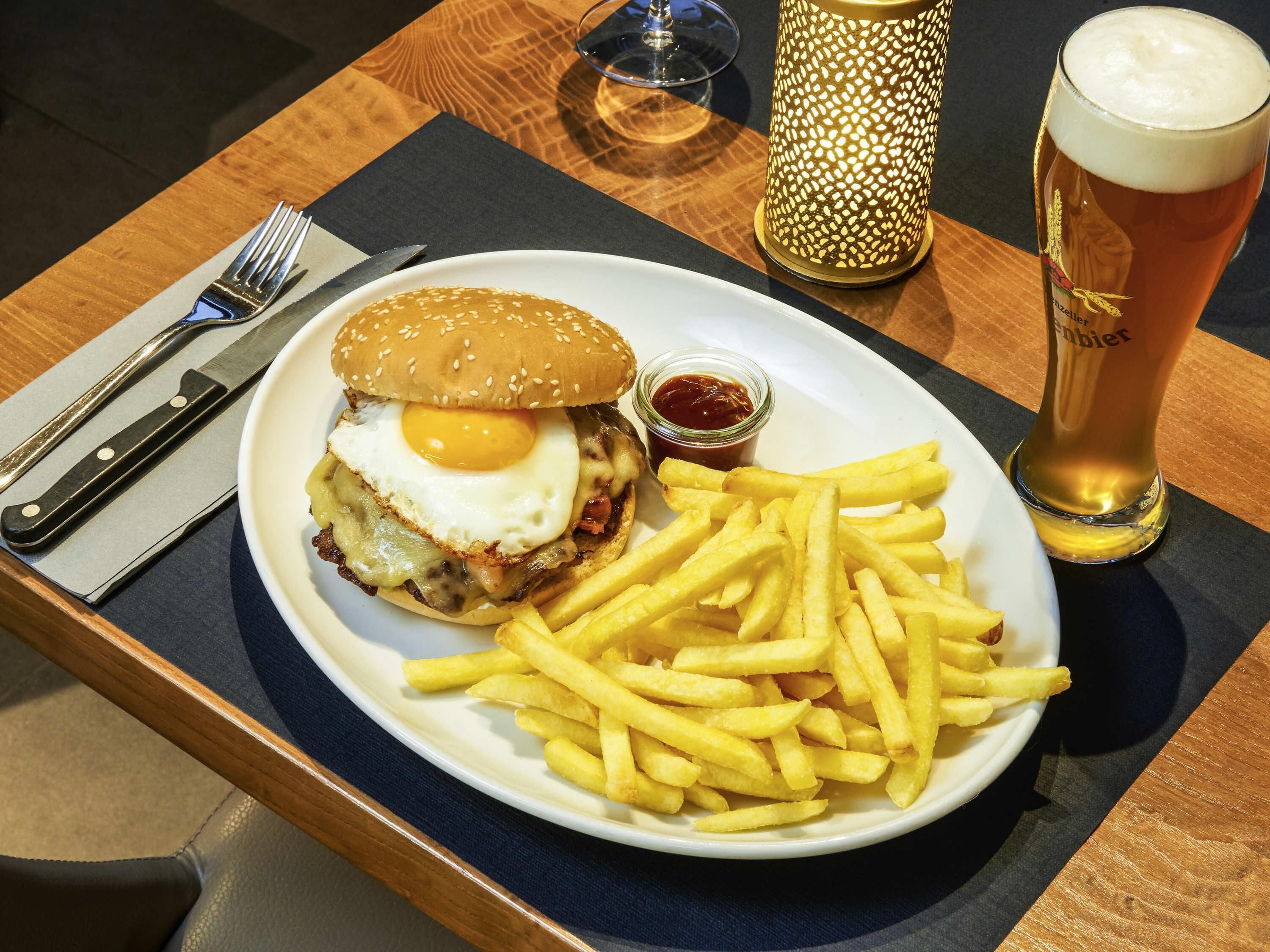 Un plato con una hamburguesa, papas fritas y una jarra de cerveza sobre una mesa.