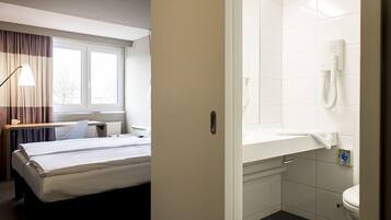 Habitación de hotel con cama, escritorio y baño con inodoro y ducha.