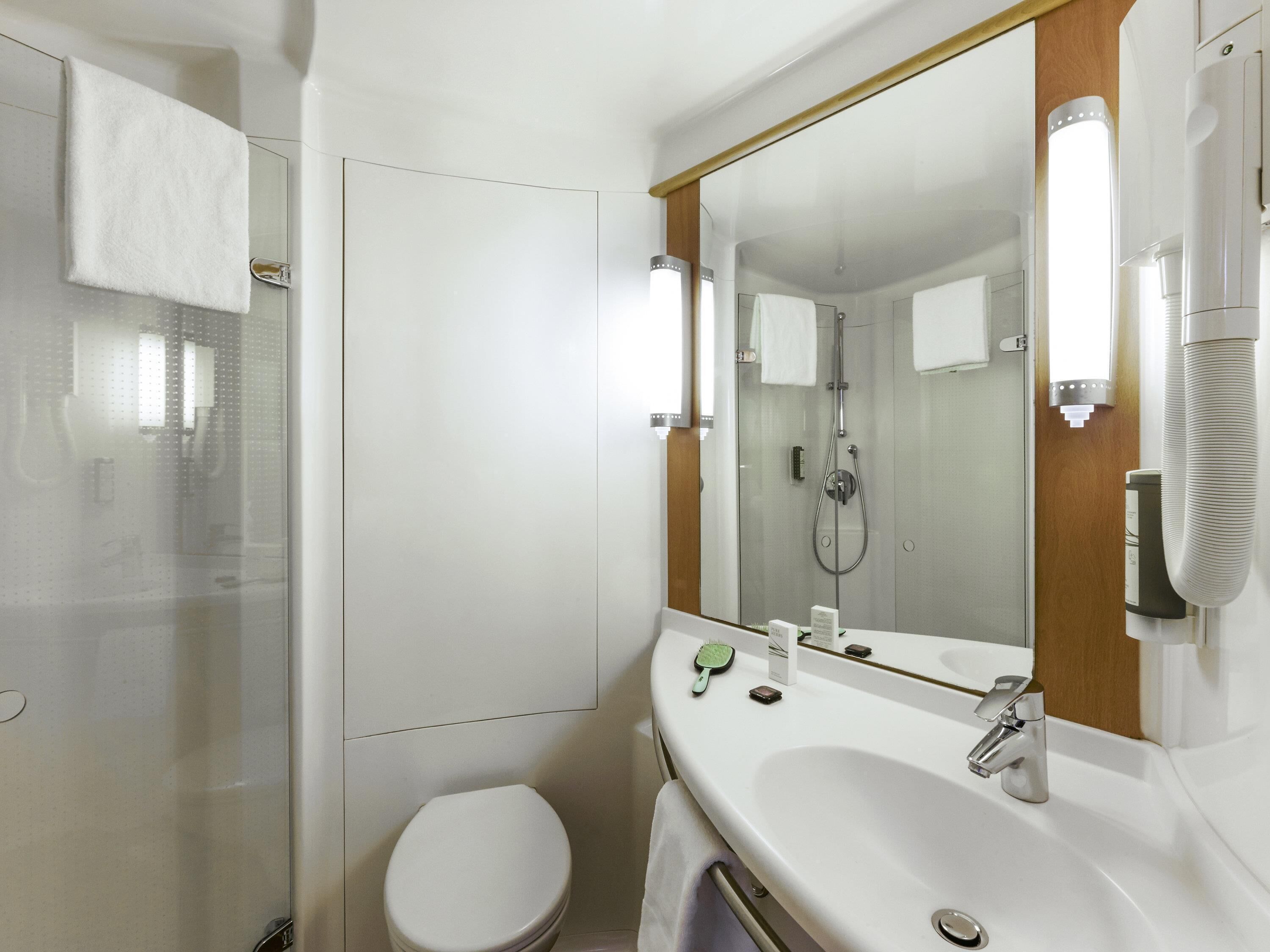 Een moderne badkamer met een douchecabine van glas, een wit toilet, een wastafel met spiegel en een handdoekrek.