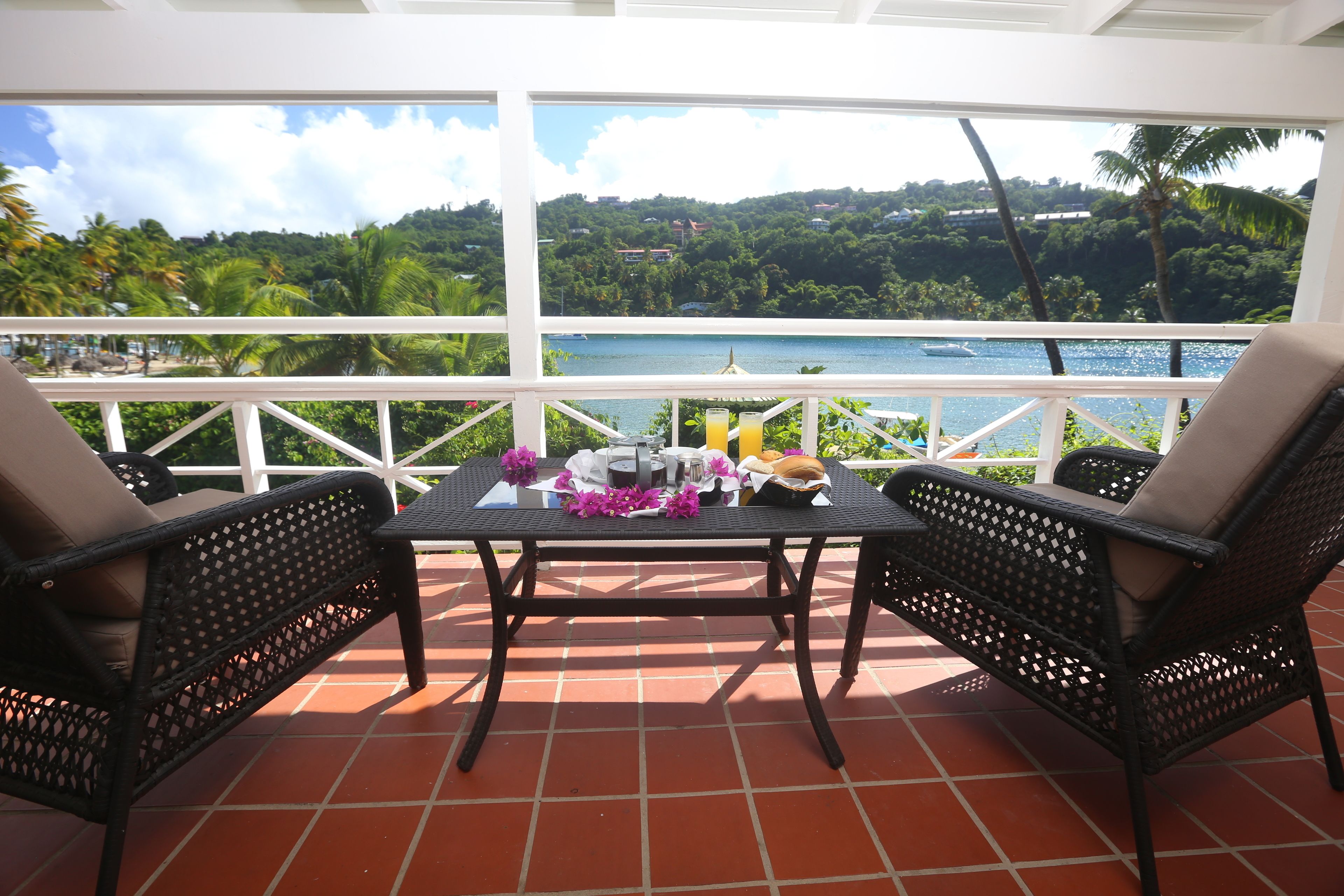 A balcony with two wicker chairs and a table, overlooking a scenic view of a lake and lush greenery.