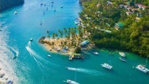 A coastal area with boats, a small island with buildings, and a forested hill.