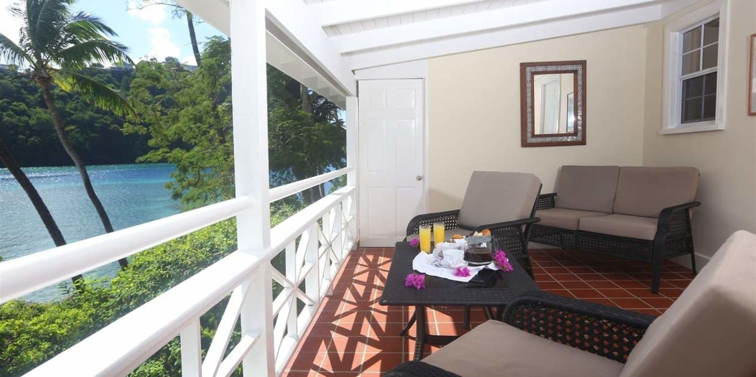 Ein Balkon mit Blick auf einen See und Palmen, ausgestattet mit einem Tisch, Stühlen und einer Couch.