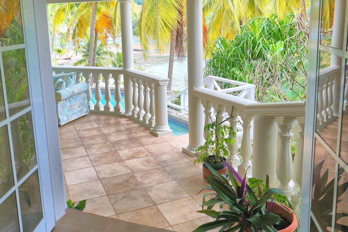 A covered balcony with a view of a pool and palm trees.
