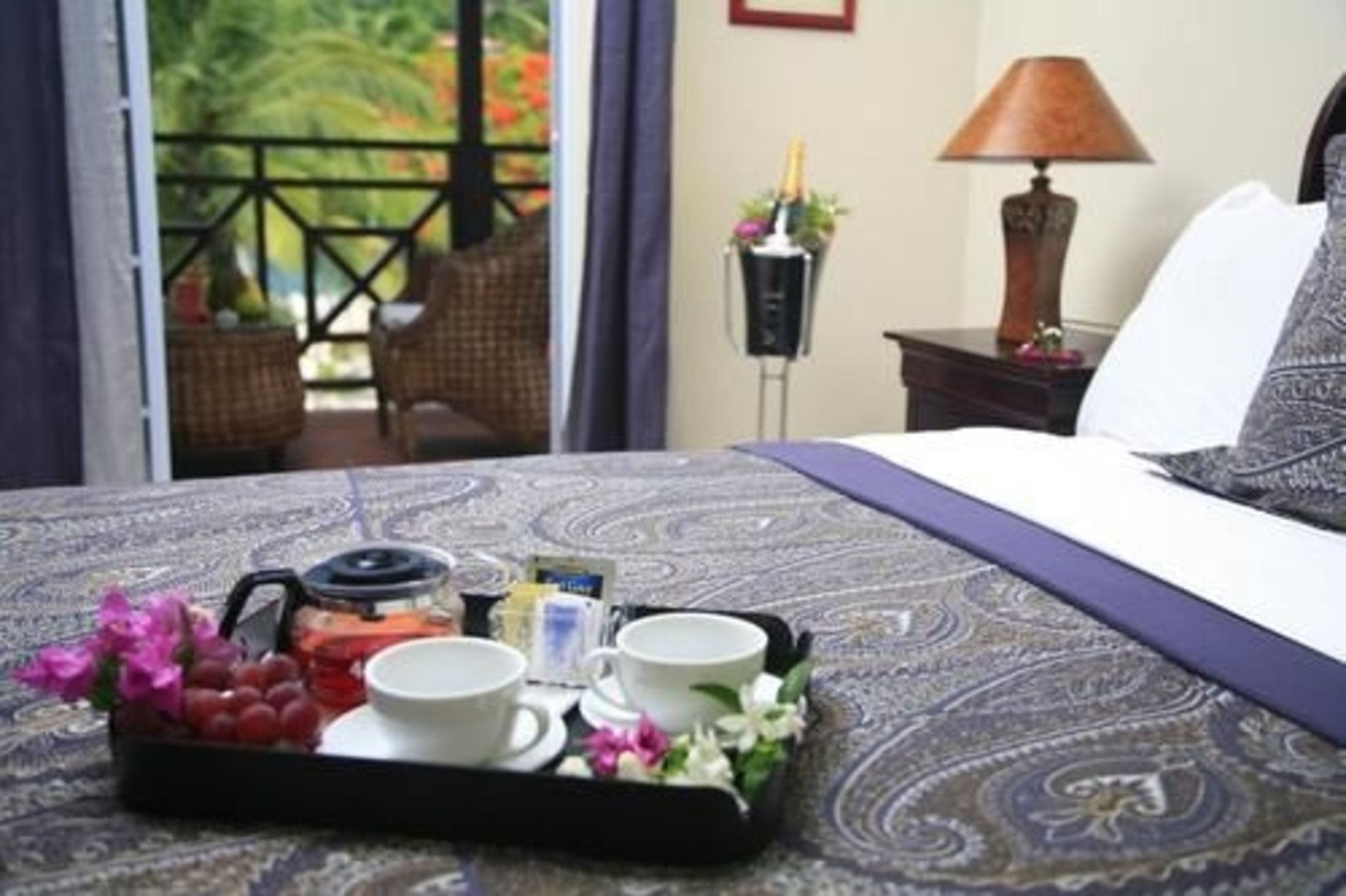 A hotel room with a bed, a tray with breakfast items, a lamp, and a view of the outdoors.