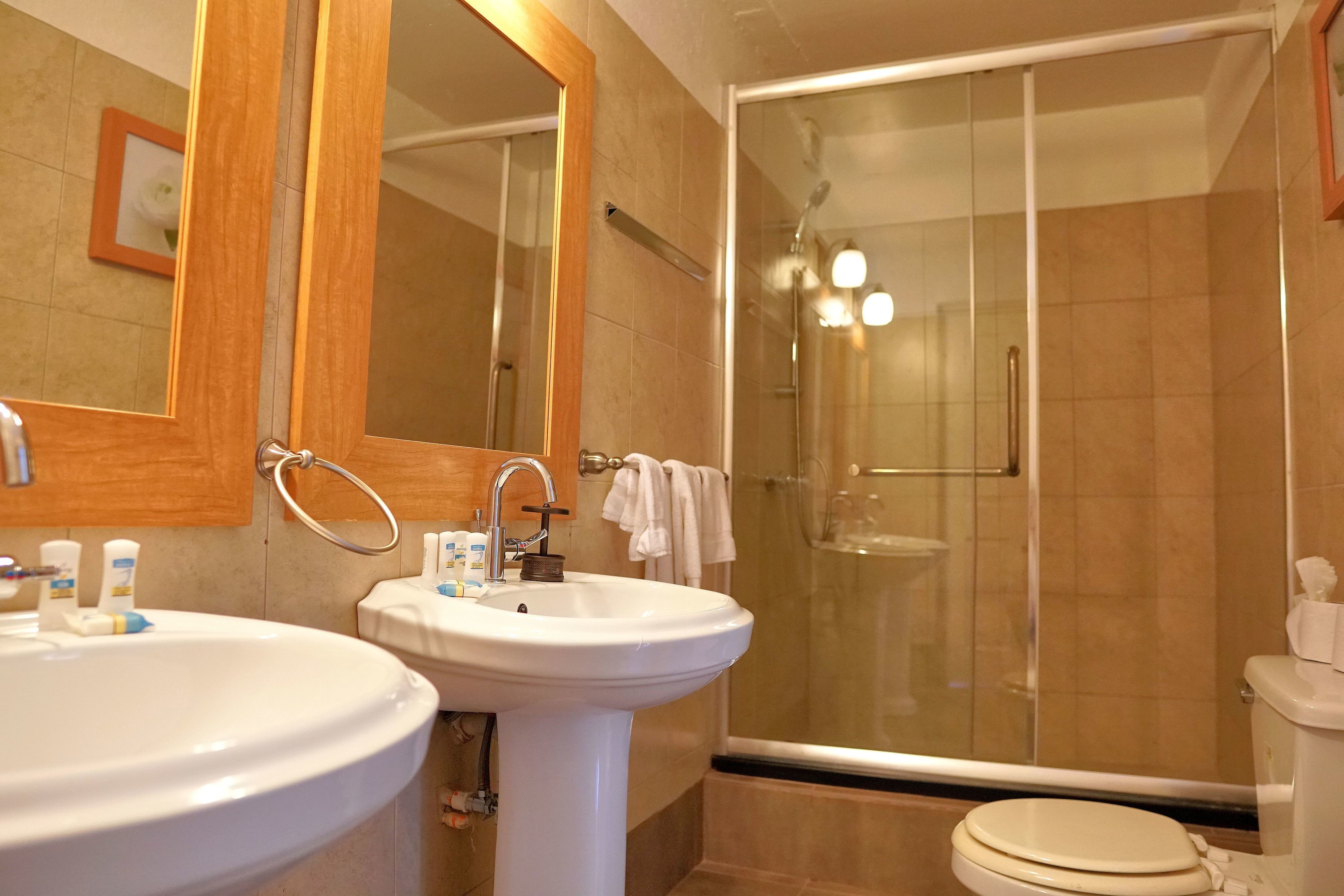 Un baño con dos lavamanos, un espejo, cabina de ducha e inodoro.