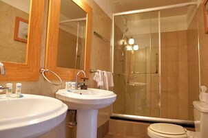 Un baño con dos lavamanos, un espejo, cabina de ducha e inodoro.