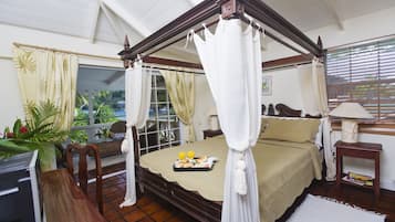 A four-poster bed with a canopy, a small bedside table with a lamp, and a view of the sea through large windows.