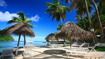 A beach with thatched umbrellas, lounge chairs, and a clear blue sky.