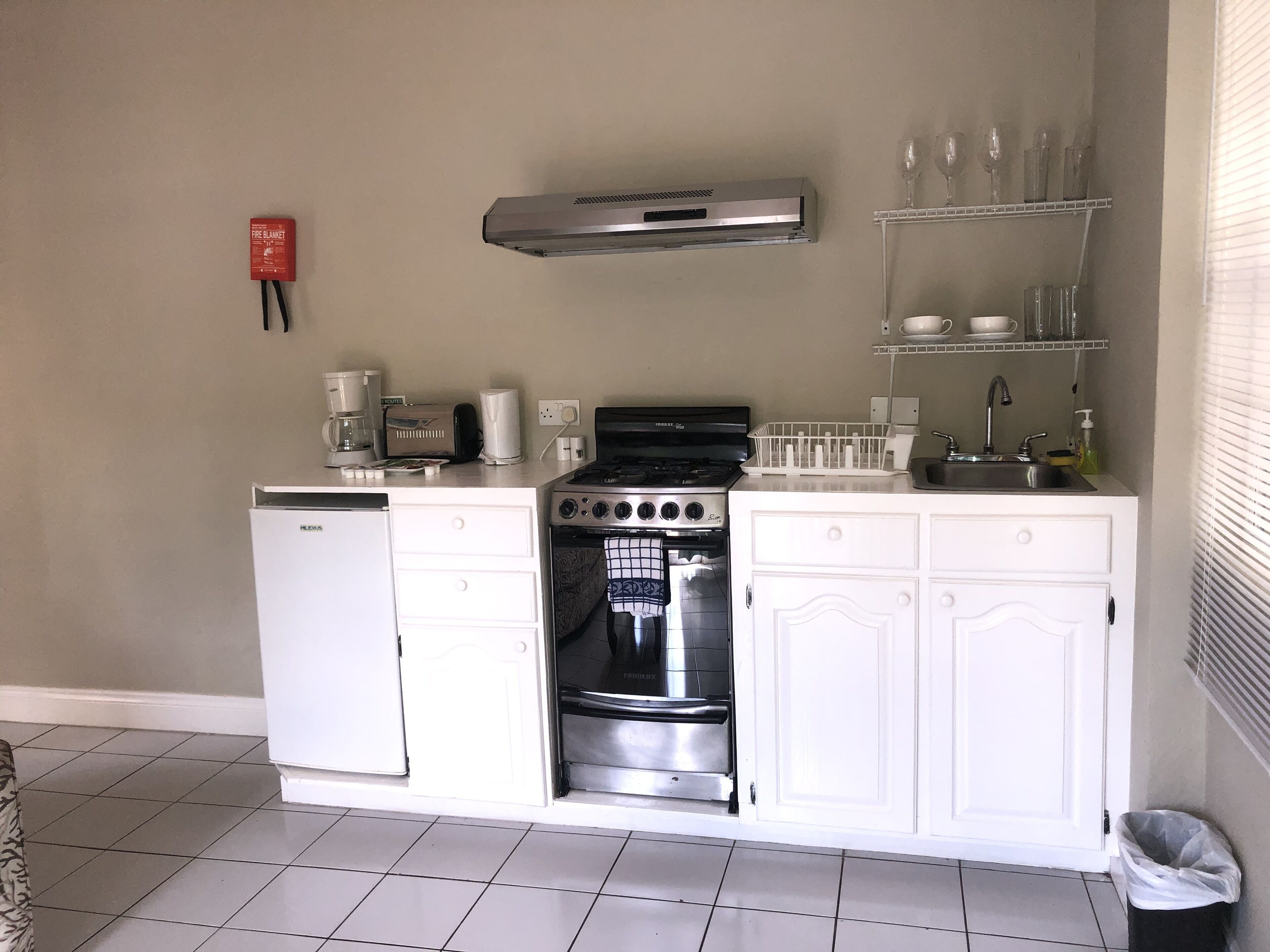 A compact kitchen with a dishwasher, stove, oven, and a small countertop area with a coffee maker and glassware.