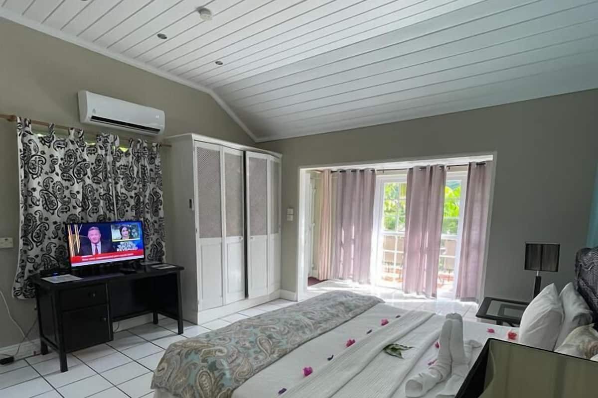 A hotel room with a bed, a desk with a computer, a TV, and a window with curtains.