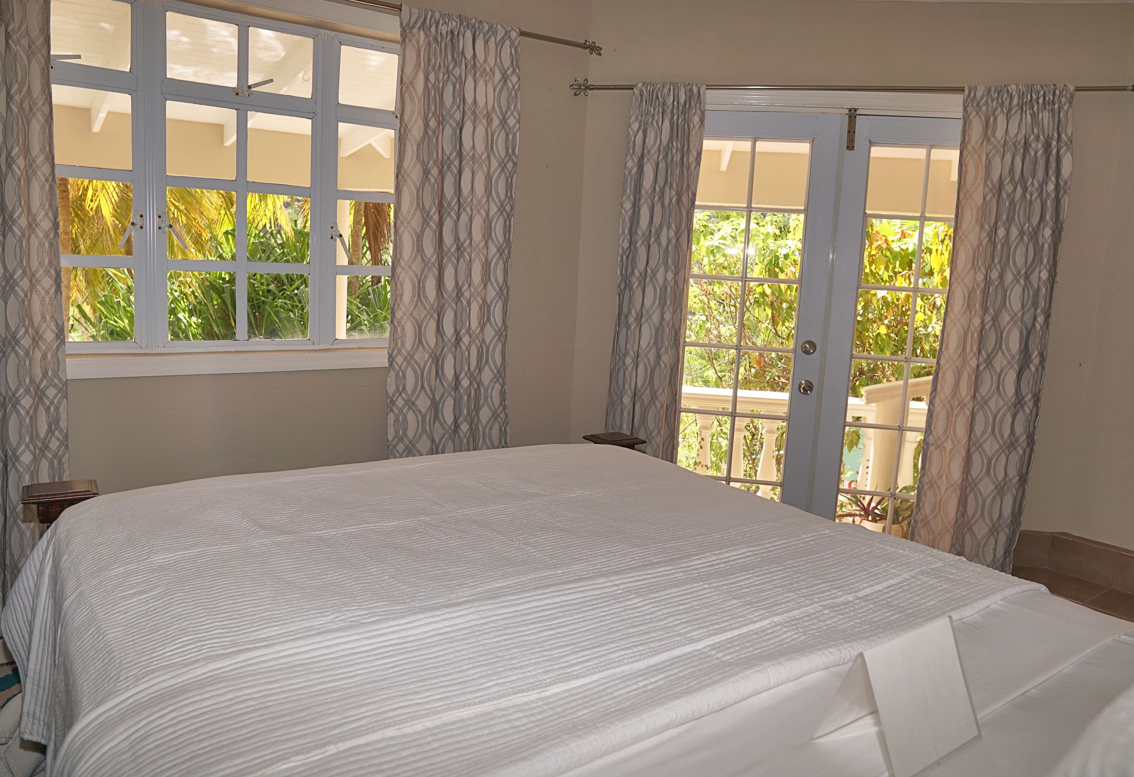A bedroom with a large bed, a window with curtains, and a door leading to an outdoor area.