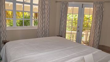 A bedroom with a large bed, a window with curtains, and a door leading to an outdoor area.